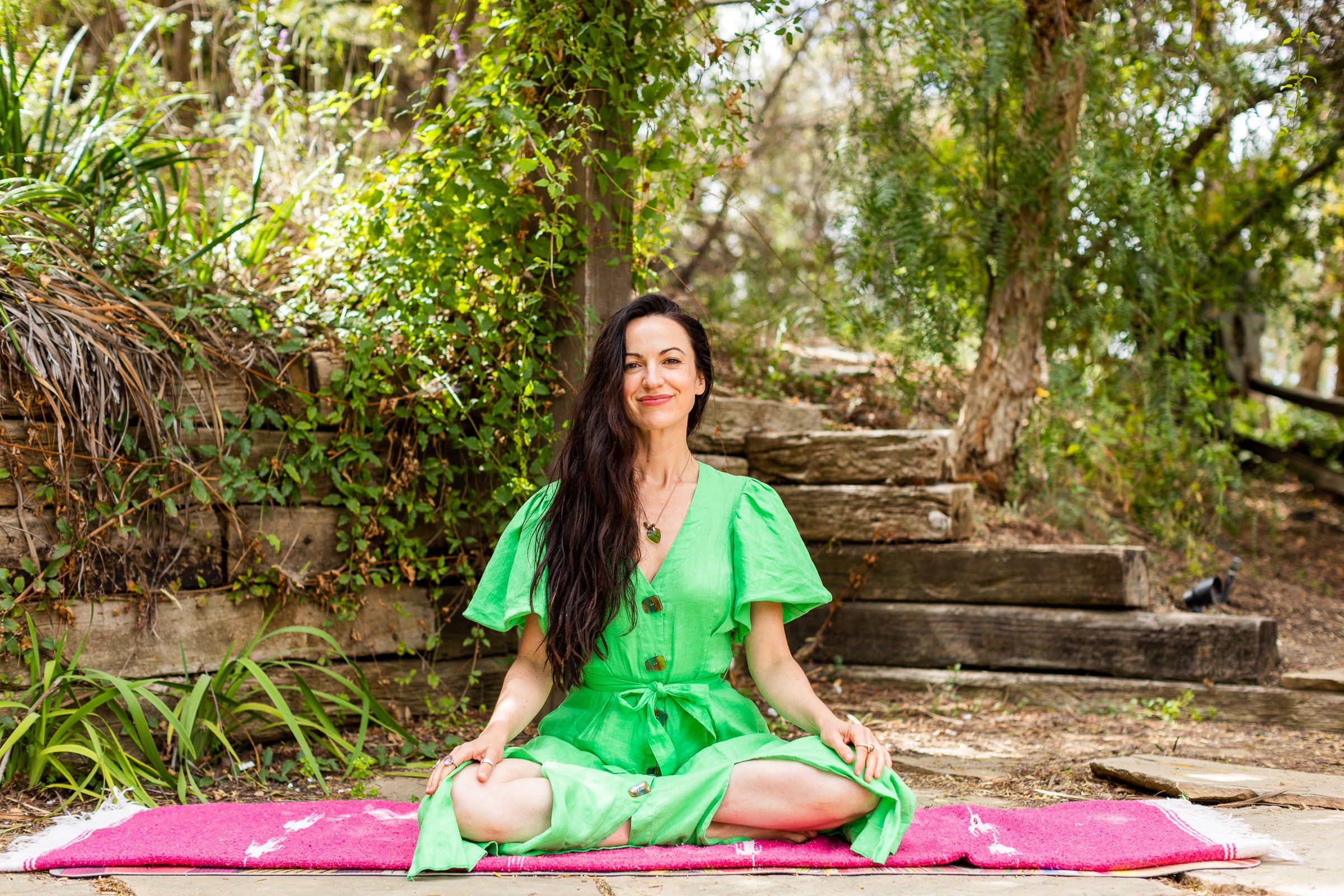 Alexandra Hulme sitting cross-legged on a pink mat in a sunlit garden