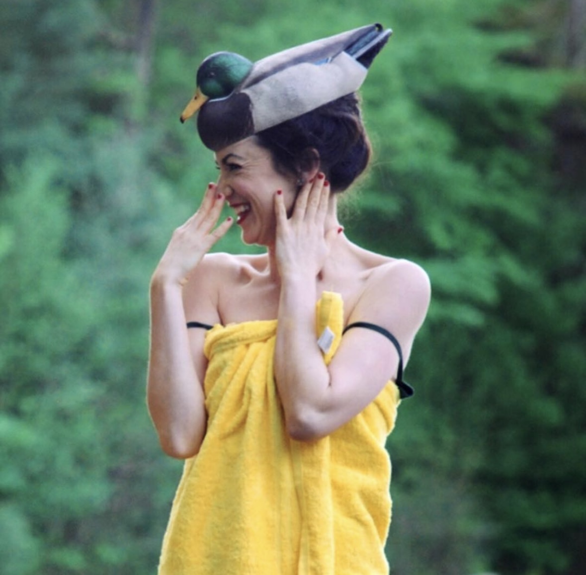 Alexandra Hulme laughing in a yellow towel and a duck-decoy hat, in the woods