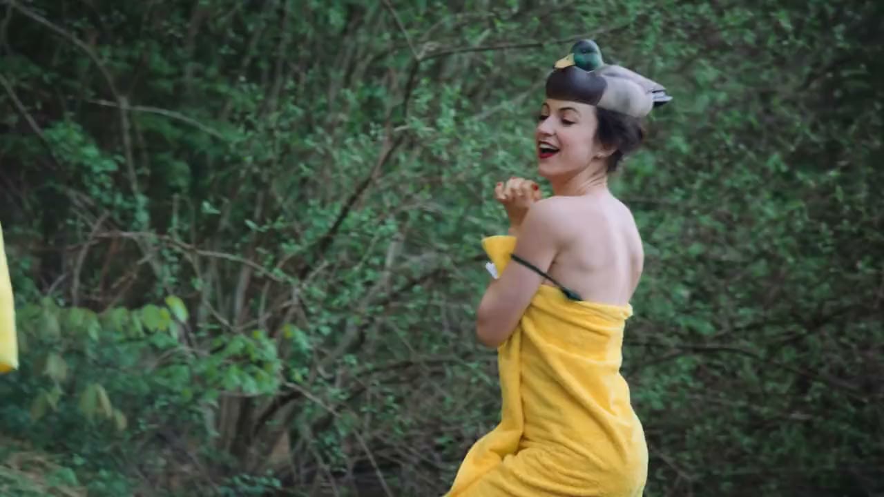 Alexandra Hulme laughing in a yellow towel and a duck-decoy hat, in woodland